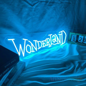 May include: A blue neon sign with the word "Wonderland" in white neon letters. The sign is on a blue fabric surface with a calendar in the background.