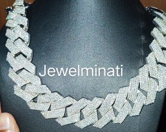 May include: A silver chain necklace with a large, chunky link design. The chain is fully iced out with small, clear stones. The necklace is displayed on a black mannequin bust. The text "Jewelminati" is visible on the bust.