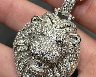 May include: A silver lion head pendant necklace with a chain. The lion's head is covered in small, clear diamonds.