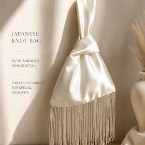 May include: A cream-colored satin Japanese knot bag featuring a long, beaded fringe detail at the bottom. The text on the image reads: JAPANESE KNOT BAG, SATIN & BEADED FRINGE DETAIL, TIMELESS ELEGANCE FOR SPECIAL MOMENTS. The bag has a single handle.