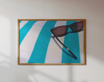 Puede incluir: Un par de gafas de sol negras con lentes marrones descansando sobre una toalla de rayas azules y blancas.