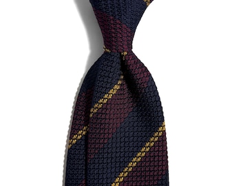 May include: A close-up of a navy blue and burgundy striped tie with a textured knit pattern. The tie features diagonal gold stripes and is knotted at the top, showcasing a classic menswear accessory.