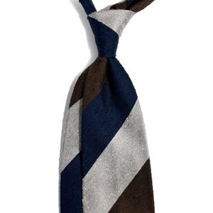 May include: A striped tie in navy blue, brown, and silver-grey. The diagonal stripes are visible on the knotted tie. The fabric's texture is evident. The background is plain white.