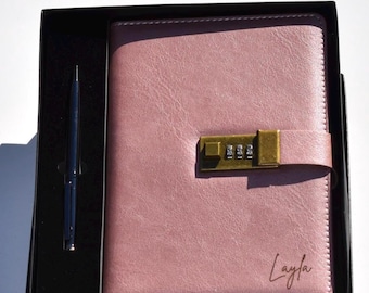 May include: A pink journal with a combination lock and a matching pen, presented in a black box. The journal has the name "Layla" written on the bottom right corner. The lock is a brass color.