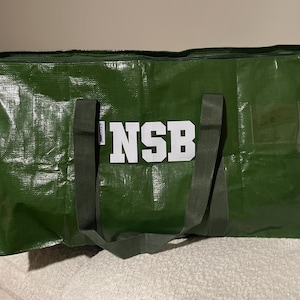 Op de afbeelding: Een grote, groene draagtas met de witte letters "NSB" op de voorkant. De tas heeft twee donkergroene handvatten en een ritssluiting. De tas is gemaakt van een duurzaam, waterdicht materiaal.