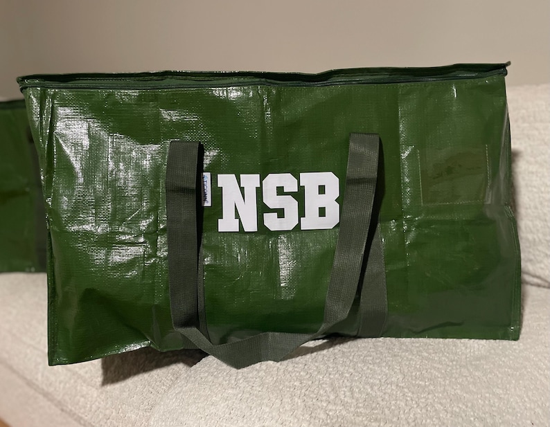 Op de afbeelding: Een grote, groene draagtas met de witte letters "NSB" op de voorkant. De tas heeft twee donkergroene handvatten en een ritssluiting. De tas is gemaakt van een duurzaam, waterdicht materiaal.