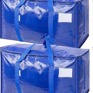 Op de afbeelding: Twee grote, blauwe opbergtassen met bijpassende blauwe handvatten en ritsen. Elke tas heeft een rechthoekige labelhouder aan de zijkant. De tassen zijn gemaakt van een glanzend, duurzaam materiaal, geschikt voor verhuizen of opslag.