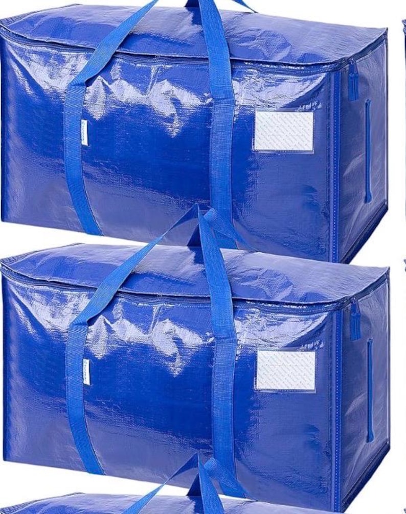 Op de afbeelding: Twee grote, blauwe opbergtassen met bijpassende blauwe handvatten en ritsen. Elke tas heeft een rechthoekige labelhouder aan de zijkant. De tassen zijn gemaakt van een glanzend, duurzaam materiaal, geschikt voor verhuizen of opslag.