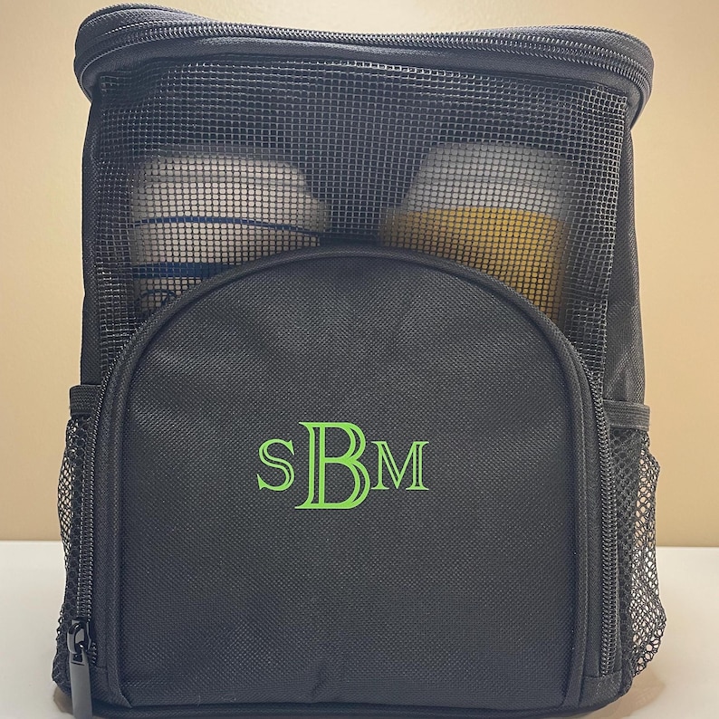 May include: A black rectangular storage bag with a top zipper closure and a mesh upper panel. The front features a semi-circular pocket embroidered with the lime green monogram letters SBM. Two side mesh pockets are attached to the main body.