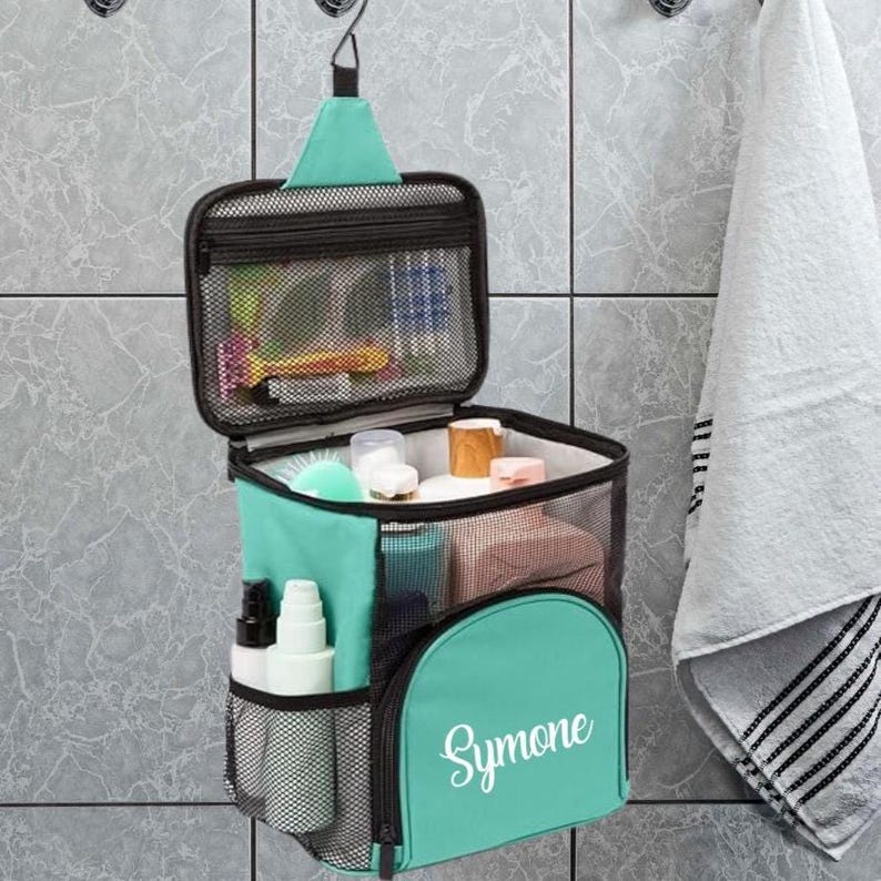 May include: A hanging teal toiletry bag with a mesh top compartment and a front pocket featuring the white text Symone. The bag includes a zippered opening, side mesh pockets, and internal storage for various personal care items.