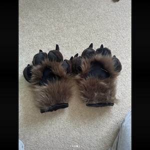 Peut inclure: Une paire de gants en forme de pattes d'animal en fausse fourrure marron et noire, dotés d'une fourrure pelucheuse marron foncé, de paumes en tissu noir et de griffes rembourrées noires bien visibles au bout de chaque doigt.