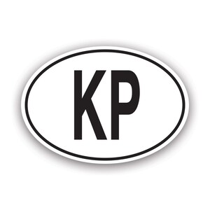 Può includere: Adesivo ovale bianco con bordo nero. L'adesivo presenta le lettere "KP" in grassetto, in nero, centrate sullo sfondo bianco. L'adesivo ha un leggero effetto ombra.