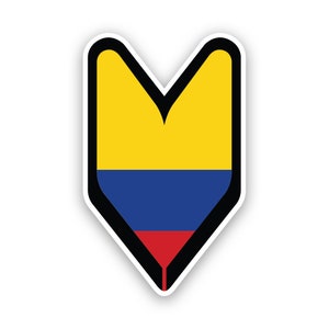 Può includere: Un adesivo raffigurante la bandiera colombiana in una forma a scudo stilizzata rivolta verso il basso. I colori della bandiera sono giallo, blu e rosso, delineati in nero. L'adesivo ha un bordo bianco e una leggera ombra.