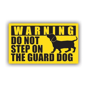 May include: A rectangular yellow sign with black text that reads "WARNING DO NOT STEP ON THE GUARD DOG." A black silhouette of a dog is on the right side of the sign.