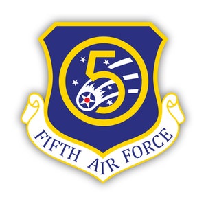Könnte beinhalten: Ein blaues und gelbes schildförmiges Emblem mit einer weißen Schriftrolle am unteren Rand. Die Schriftrolle lautet "FIFTH AIR FORCE". Das Schild hat einen gelben Kreis mit einer weißen Zahl "5" und einen weißen Kometen mit fünf Sternen darin.