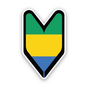 Può includere: Un adesivo per targhe giapponese per conducenti principianti, di colore verde, giallo e blu. L'adesivo ha la forma di un cuore ed è bordato di nero.