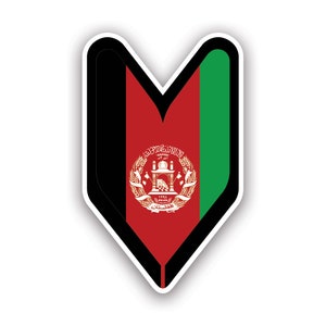 May include: A sticker in the shape of a downward-pointing shield, featuring the flag of Afghanistan. The flag design includes vertical stripes of black, red, and green, with the national emblem centered on the red stripe. The sticker has a white border.