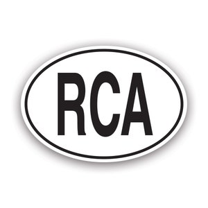 May include: Oval sticker with the letters "RCA" in bold black font, centered on a white background. The sticker has a thin black border and a subtle drop shadow, giving it a raised appearance. The design is simple and clean.