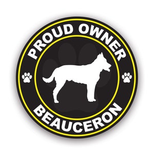 May include: A round black sticker with a yellow border and white text that reads "PROUD OWNER BEAUCERON". The sticker features a white silhouette of a Beauceron dog, paw prints, and a black background.