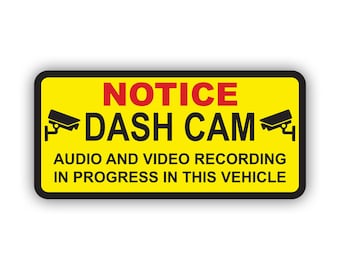 May include: Yellow and black warning sign with the text "NOTICE DASH CAM AUDIO AND VIDEO RECORDING IN PROGRESS IN THIS VEHICLE". The sign has two black and white camera icons on either side of the text.
