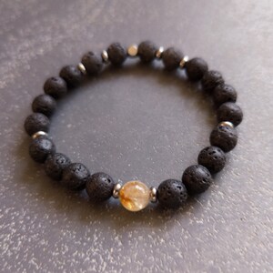 Könnte beinhalten: Ein Armband aus schwarzem Lavastein mit einer einzigen goldenen Citrinperle und silbernen Abstandshaltern.