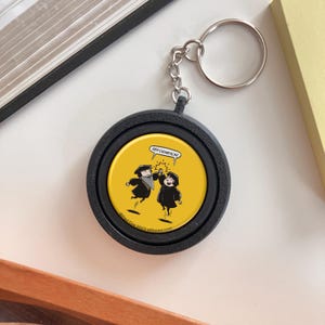 May include: A round black keychain featuring a yellow circular insert with a cartoon illustration of two figures in black robes high-fiving. A speech bubble above them contains the text REFORMATION. The copyright text Paul Cox 2023 reftoons.com is printed at the bottom.