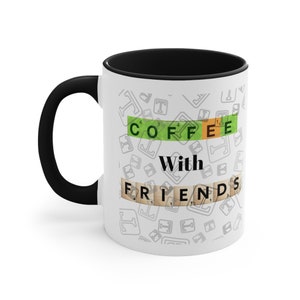 May include: White ceramic coffee mug with a black handle and interior. The mug features the words "COFFEE With FRIENDS" in a Scrabble-like design. The background has a pattern of gray letter tiles.