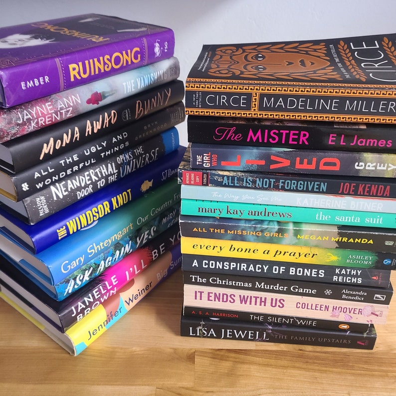 May include: A stack of paperback books with various titles and authors. The books are arranged vertically, with the top book being "Circe" by Madeline Miller. The books are all different colors and have different designs.