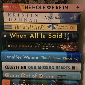 May include: A stack of ten paperback books with blue, green, yellow, and white covers. The titles of the books are visible: "The Hole We're In", "Night Road", "The Jetsetters", "When All Is Said", "All the Ugly and Wonderful Things", "The Summer Place", "Our Missing Hearts", "Oona Out of Order", and "Little Fires Everywhere".
