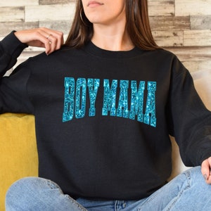 May include: Black sweatshirt with the text "BOY MAMA" in a sparkling, light blue, block letter design. The sweatshirt is a crew neck style and is made of a soft material.
