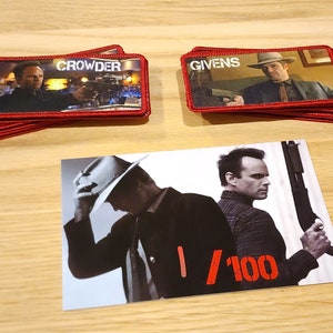 May include: Two red fabric patches with the names "Crowder" and "Givens" printed on them. A photo of two men, one wearing a cowboy hat, with the text "1/100" printed on the photo.
