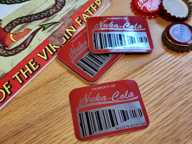 Może przedstawiać: Trzy czerwone prostokątne naklejki z tekstem "PROPERTY OF Nuka-Cola" i kodem kreskowym. Tekst "NCC2078-02147-030" jest nadrukowany pod kodem kreskowym na każdej naklejce.