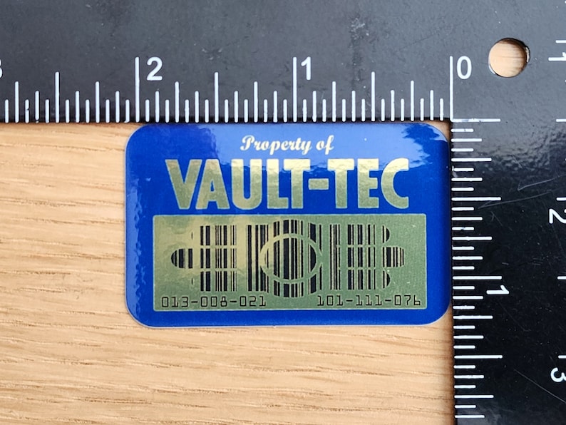 K&ouml;nnte beinhalten: Ein blauer und goldener Aufkleber mit dem Text "Property of Vault-Tec" und einem Barcode. Der Aufkleber tr&auml;gt die Nummern "013-008-021" und "101-111-076".
