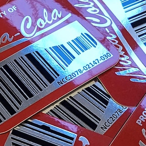 Puede incluir: Pegatinas rojas y plateadas con el texto "Nuka-Cola" y un código de barras. El número del código de barras es NCC2078-02147-030. Las pegatinas están etiquetadas como "Property of".
