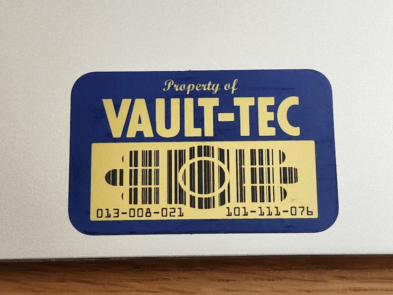 K&ouml;nnte beinhalten: Ein blauer und goldener Aufkleber mit dem Text "Property of VAULT-TEC" und einem Barcode mit den Nummern "013-008-021" und "101-111-076".