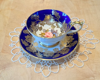 May include: A white teacup and saucer with a floral design and gold trim. The saucer and cup are decorated with a cobalt blue background and gold accents.