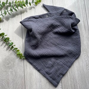 Könnte beinhalten: Ein dunkelgraues Musselin-Baby-Bandana-Lätzchen mit zwei Druckknöpfen. Das Lätzchen ist aus weichem, atmungsaktivem Stoff gefertigt und perfekt, um die Kleidung des Babys sauber zu halten.
