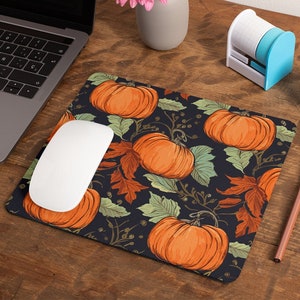 May include: A dark blue mouse pad with a repeating pattern of orange pumpkins, green leaves, and brown branches. The mouse pad is on a wooden surface.