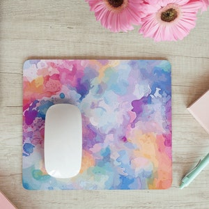 May include: A colorful abstract watercolor mouse pad with a white computer mouse on top. The mouse pad has shades of pink, purple, blue, yellow, and orange.