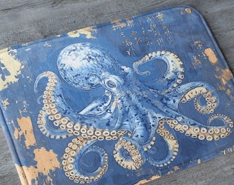 May include: A blue and white octopus with yellow tentacles on a blue and beige bath mat. The octopus is in the centre of the mat and has a distressed, vintage look.