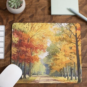 May include: A mouse mat featuring a watercolour painting of a path through an autumnal forest. The trees are a mix of yellow, orange and red.