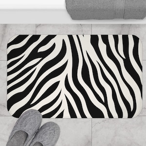 May include: Black and white zebra patterned bath mat. The mat is rectangular and has a soft, absorbent surface.
