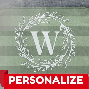 Könnte beinhalten: Eine rechteckige Badematte mit gestreiftem grünem Hintergrund. Ein weißer Blumenkranz umgibt den Buchstaben "W" in der Mitte. Das Wort "PERSONALISIEREN" wird in weißer Schrift auf einem roten Banner unten angezeigt.