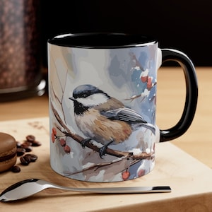 May include: A black and white mug with a winter scene featuring a small bird perched on a branch with red berries. The mug has a black rim and handle.