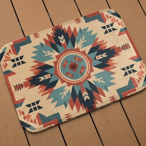 May include: A beige rug with a geometric pattern in shades of red, blue, and black. The pattern is reminiscent of Native American art.