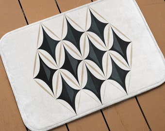 May include: A white bath mat with a geometric pattern of black and beige triangles and ovals. The pattern is centered on the mat.