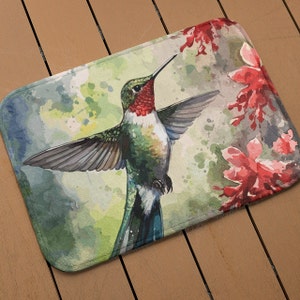 May include: A watercolor painting of a hummingbird with red, green, and blue feathers hovering near pink flowers. The background is a soft green and yellow watercolor wash.
