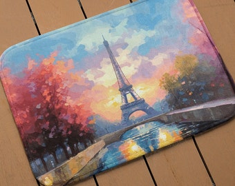 Op de afbeelding: Een kleurrijke deurmat met een schilderij van de Eiffeltoren in Parijs, Frankrijk. Het schilderij toont de toren in de verte met een brug en een rivier op de voorgrond. De lucht is een levendige blauwe kleur met roze en oranje wolken.