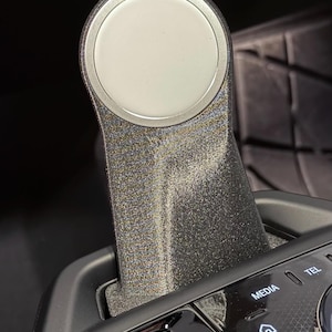 May include: A close-up of a black car's gear shifter with a silver knob. The shifter has a textured surface and is surrounded by black plastic. The word "START STOP" is visible on a button below the shifter.