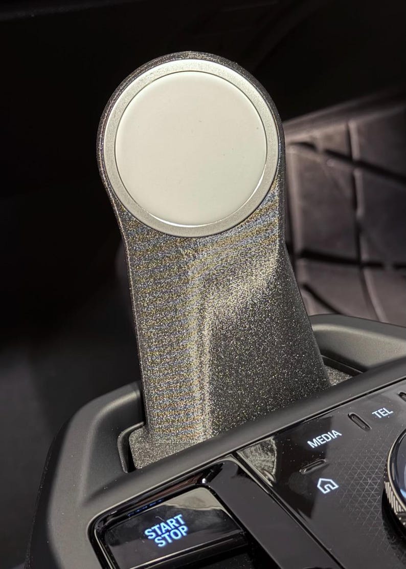 May include: A close-up of a black car's gear shifter with a silver knob. The shifter has a textured surface and is surrounded by black plastic. The word "START STOP" is visible on a button below the shifter.